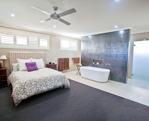 Interior of a contemporary bedroom featuring a freestanding bathtub, black accent wall, and ample na.